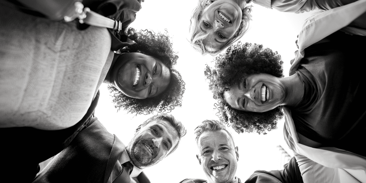 A diverse group of people smiling joyfully while standing in a circle, showcasing camaraderie and happiness.