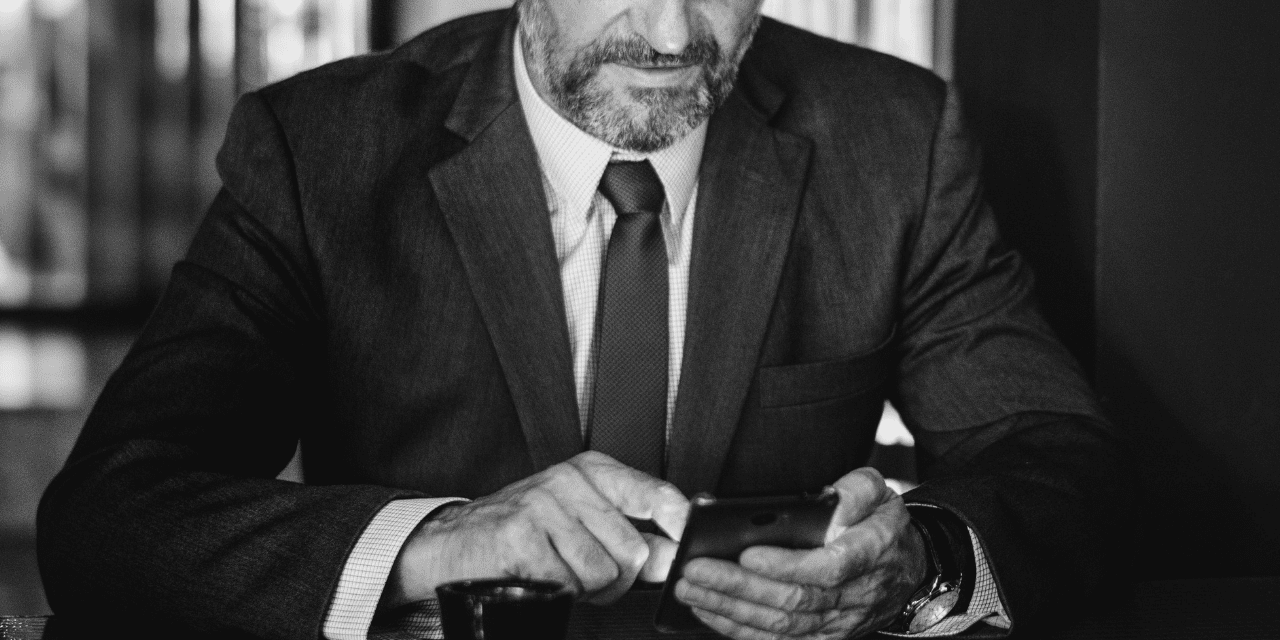 A man in a suit is intently looking at his phone, appearing focused and engaged with the device.