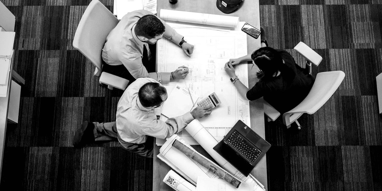 A diverse group of individuals gathered around a table, engaged in discussion with papers spread out before them.