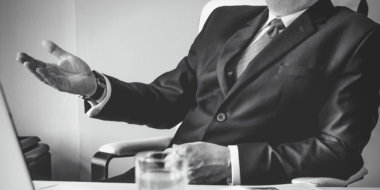Man in suit talking with his hands sitting in a desk