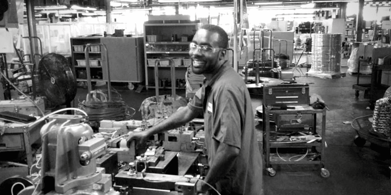 A man in a workshop operates machinery, surrounded by tools and equipment