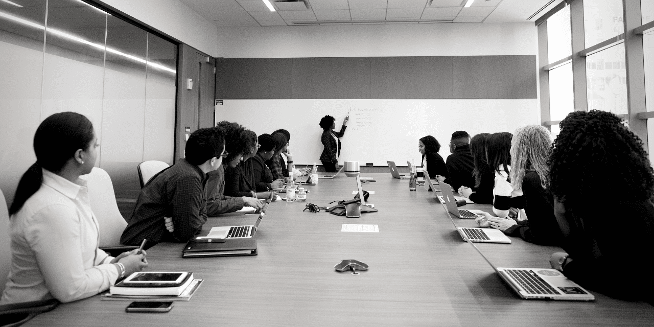 A diverse group of professionals engaged in discussion around a large conference table in a modern meeting room.