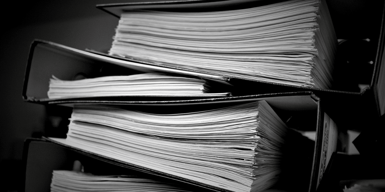 Black and white image of stacked files and documents in binders.