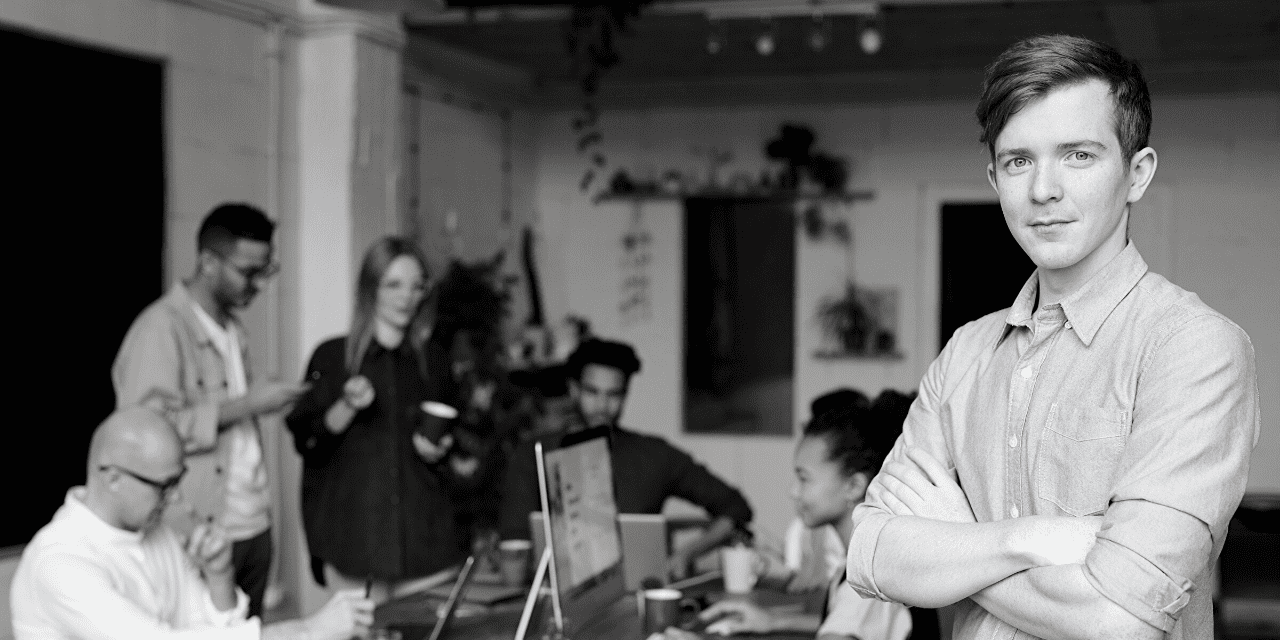 A man stands confidently before a group of attentive individuals, engaging them with his presence and message.