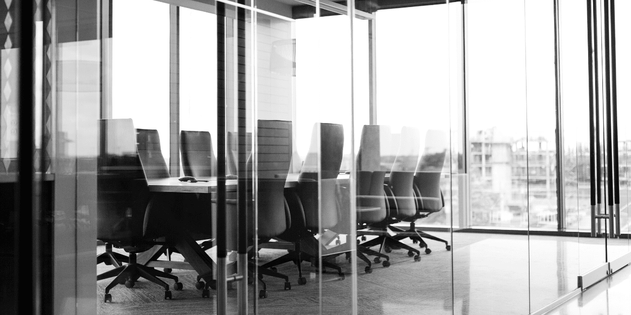 A black and white image depicting a spacious conference room with a long table and chairs arranged for a meeting.