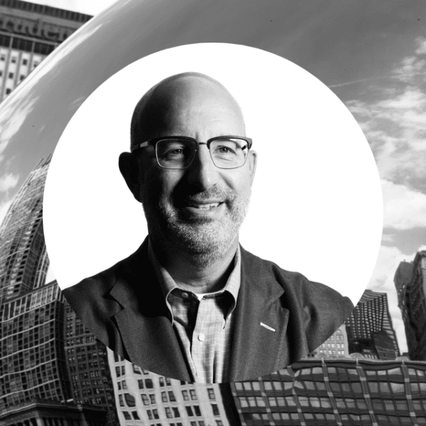 Larry in a suit and glasses stands confidently in front of a large bean sculpture, showcasing a unique artistic display.
