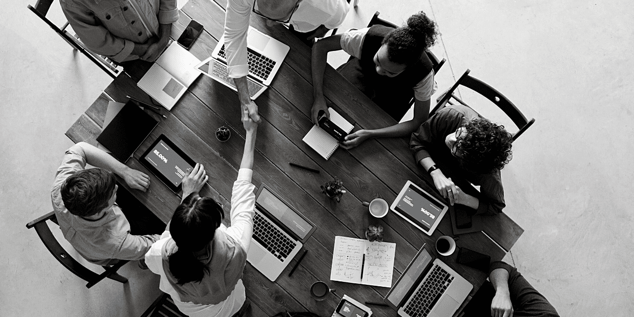 A diverse group of individuals collaborates around a table, each using a laptop for discussion and teamwork.