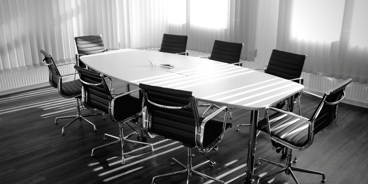 A black and white image depicting a conference table set for a meeting, showcasing its sleek design and empty chairs.