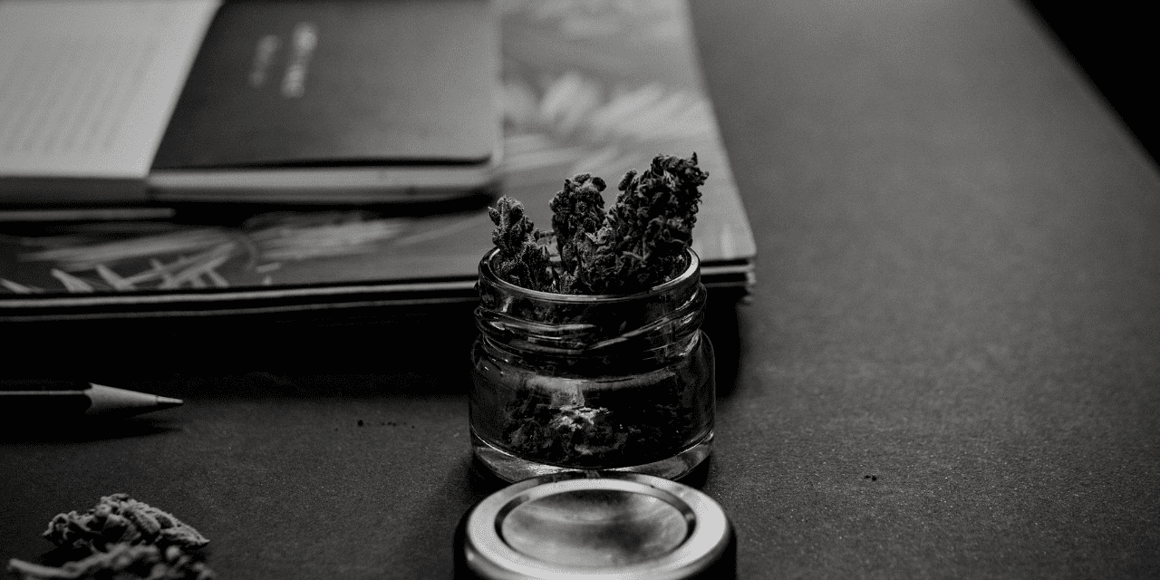 A black and white image featuring a jar filled with marijuana, showcasing its texture and form in a minimalist style.