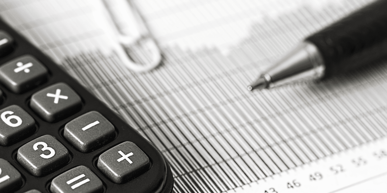 A calculator and pen on a financial spreadsheet in monochrome.