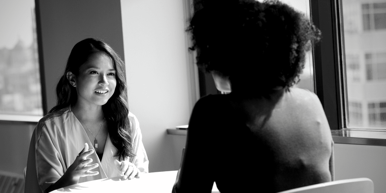 A woman engaged in conversation with another woman while seated at a table, showcasing a moment of connection.