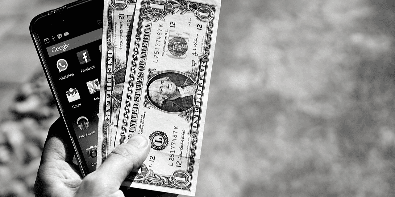 A person holding a cell phone in one hand and cash in the other, symbolizing financial transactions or mobile payments.
