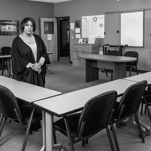 A woman stands confidently in a conference room filled with chairs and tables, ready for a meeting or presentation.