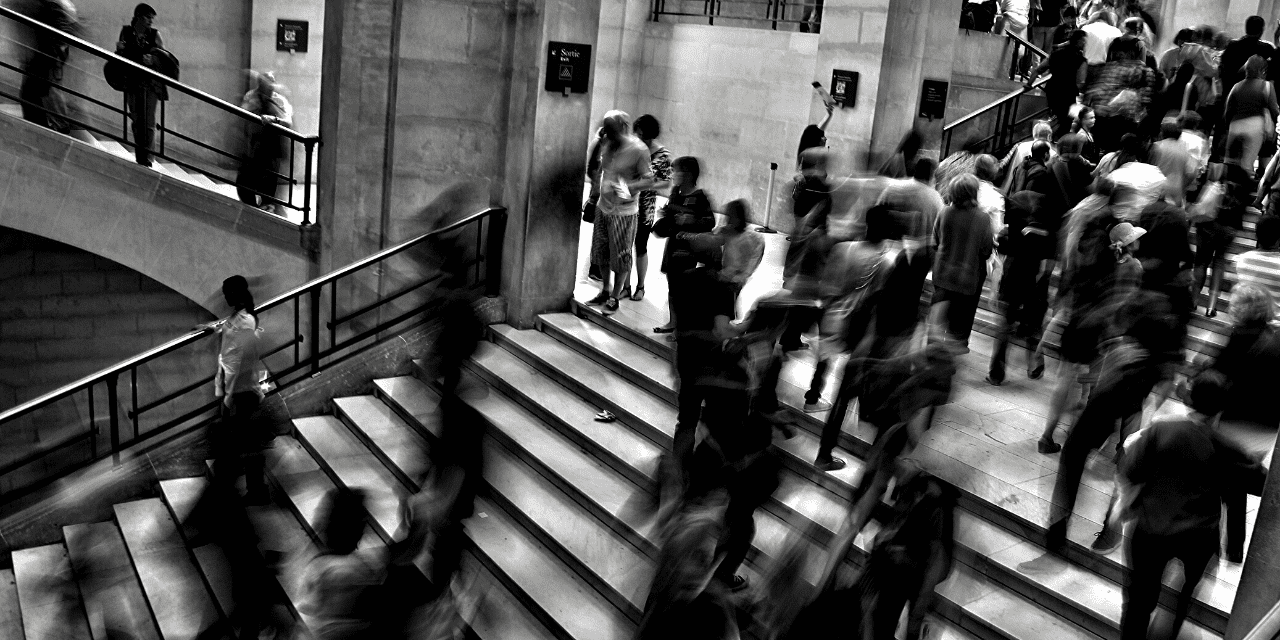 A black and white image depicting individuals descending a staircase, capturing their movement and the play of light and shadow.
